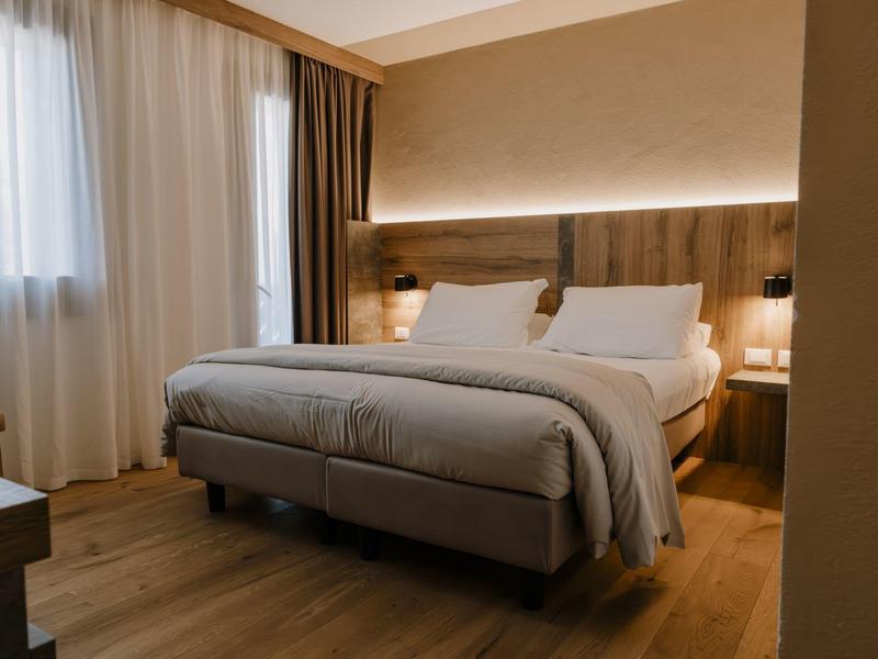 Moderní hotelový pokoj s velkou postelí, dřevěnou podlahou a závěsy u oken.