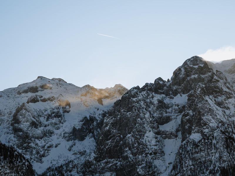 Sněhem pokryté horské vrcholy pod jasnou oblohou s slunečním světlem na vrcholcích.