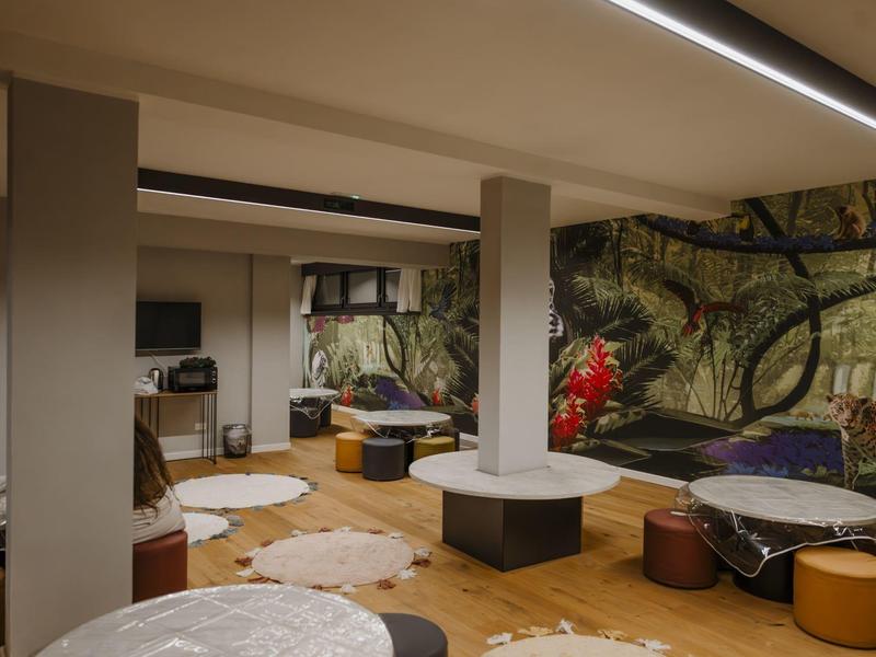 Pohodlná hotelová lounge s kulatými stoly, stoličkami a nástěnnou malbou s přírodním motivem