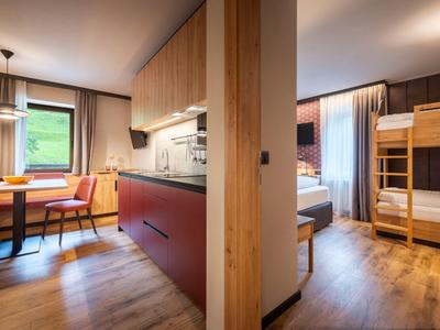 Chambres d'hôtel modernes avec coin repas, lit double et lits superposés, sol en bois et grandes fenêtres.