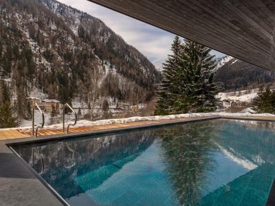 Piscine à débordement avec vue sur des montagnes boisées enneigées sous un ciel nuageux.