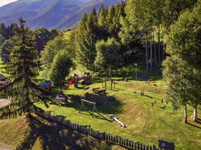 Aire de jeux verte avec balançoires et arbres environnants dans un paysage montagneux.