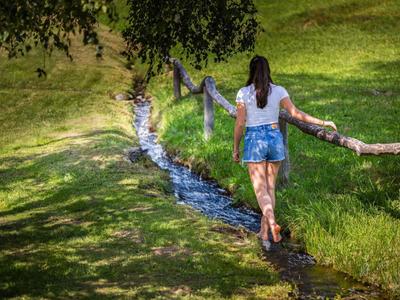 Femme qui marche sur une clôture le long d'un petit ruisseau dans un paysage verdoyant.
