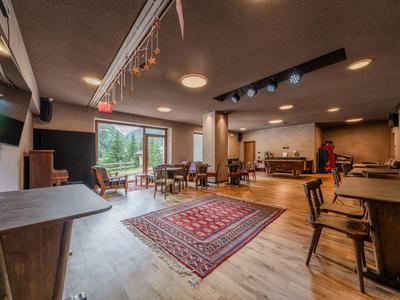 Salle à manger confortable avec mobilier en bois, tapis et grandes fenêtres donnant sur la verdure.