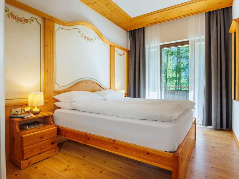 Chambre d'hôtel confortable avec mobilier en bois, grand lit et vue sur la nature verte.