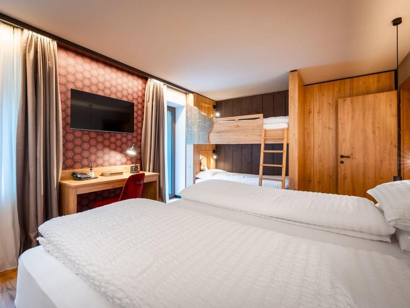 Chambre d'hôtel avec deux lits simples, lit superposé, bureau et télévision dans un décor en bois chaleureux.