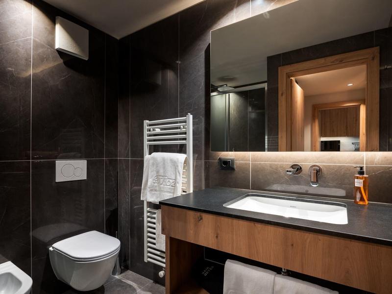 Salle de bain moderne avec carrelage foncé, miroir éclairé et meuble sous-vasque en bois.