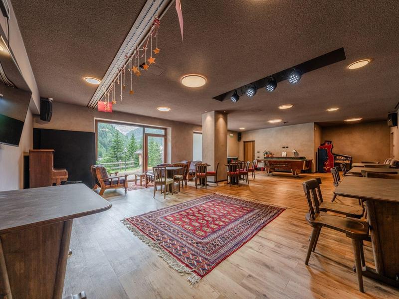 Salle à manger confortable avec mobilier en bois, tapis et grandes fenêtres donnant sur la verdure.