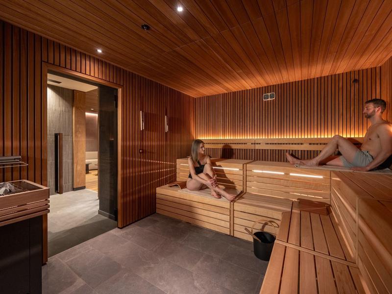 Intérieur d'un sauna moderne avec deux personnes se détendant sur des bancs en bois.