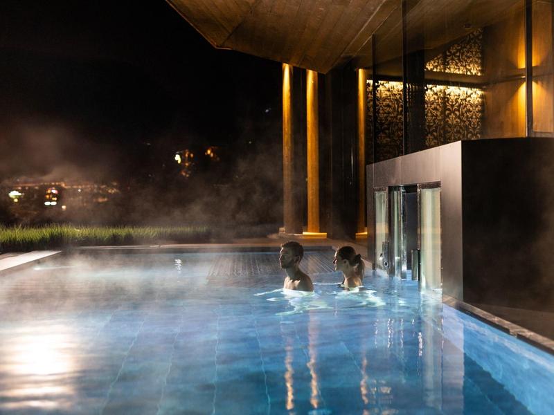 Piscine extérieure chauffée la nuit avec éclairage chaud et vapeur, des personnes dans l'eau.