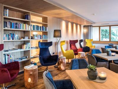 Gezellige hotellounge met kleurrijke fauteuils, boekenrekken en grote ramen.