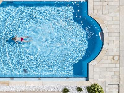 Une personne nage dans une piscine bleue claire avec une bordure en pierre vue d'en haut.