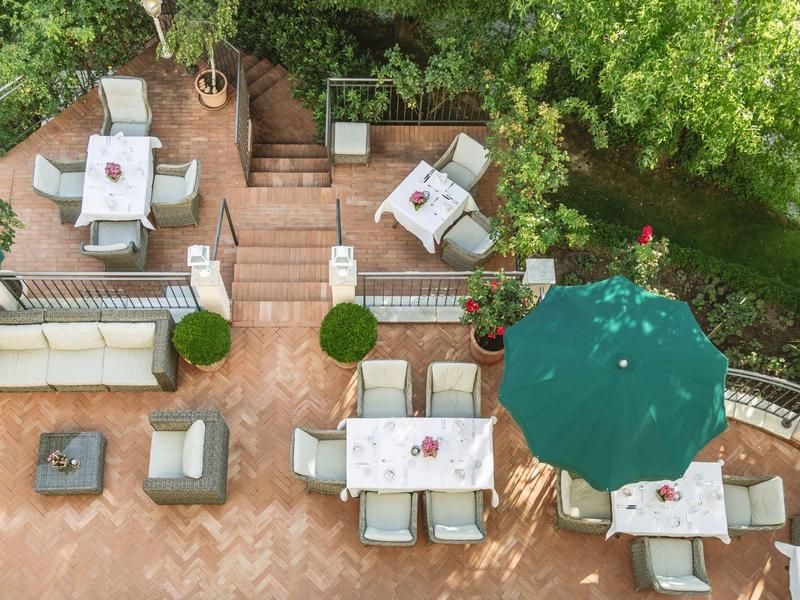 Vue de dessus d'une terrasse avec des tables, des chaises et un parasol vert entouré d'arbres.