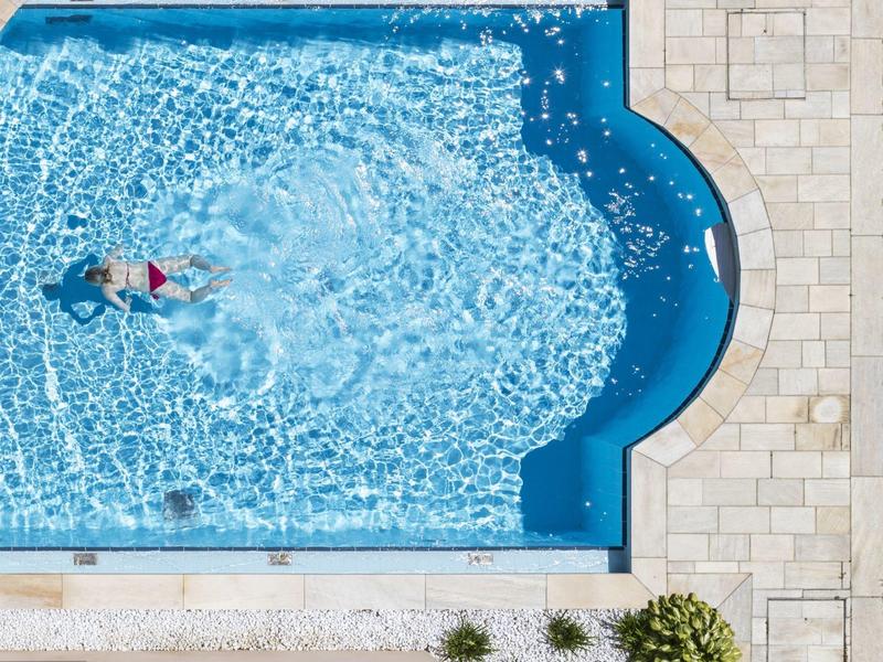 Une personne nage dans une piscine bleue claire avec une bordure en pierre vue d'en haut.