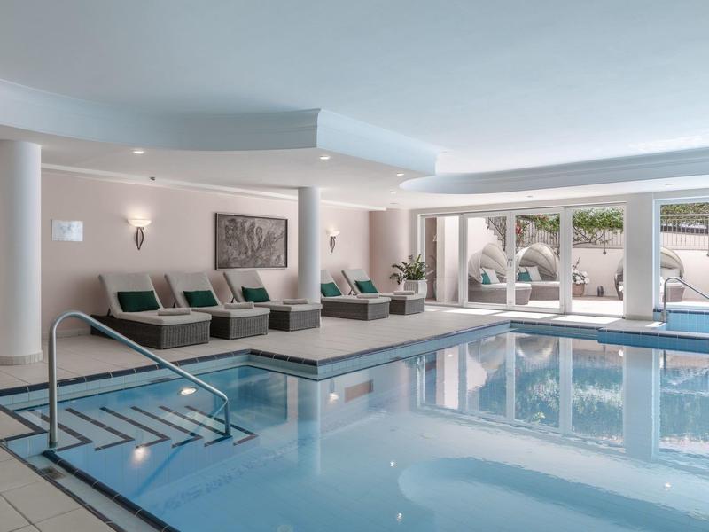 Piscine intérieure d'hôtel avec chaises longues et grandes fenêtres donnant sur l'extérieur.