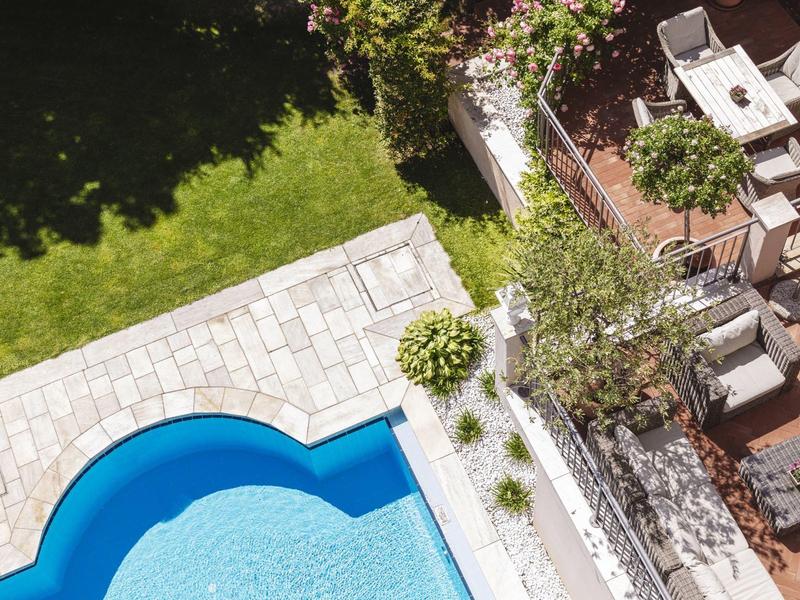 Vue aérienne d'une piscine à côté d'une terrasse avec des places assises et un jardin.