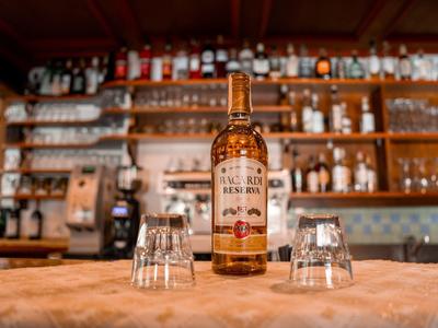 Eine Whiskyflasche und zwei Gläser auf einem Holztresen in einer Bar mit Regalen im Hintergrund.