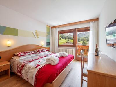 Helles Hotelzimmer mit Doppelbett, Balkon und Blick auf grüne Hügel.