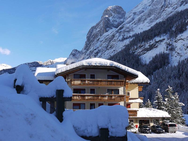 Schneebedecktes Hotelgebäude vor bewaldeten Bergen unter klarem Himmel.