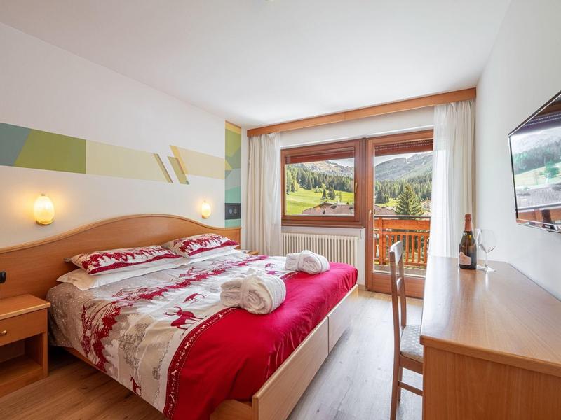 Helles Hotelzimmer mit Doppelbett, Balkon und Blick auf grüne Hügel.