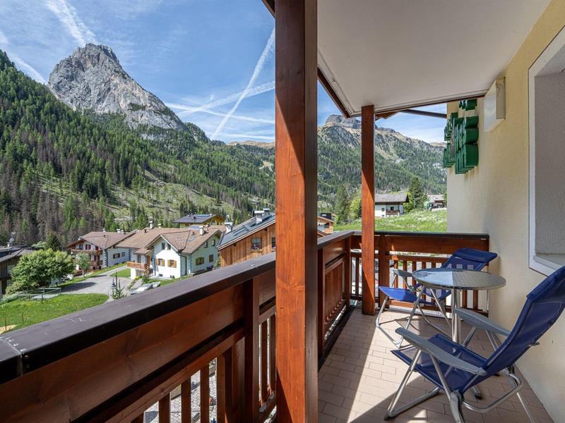 Balkon mit Stühlen und Tisch, Blick auf Berglandschaft und Dorf bei klarem Wetter.