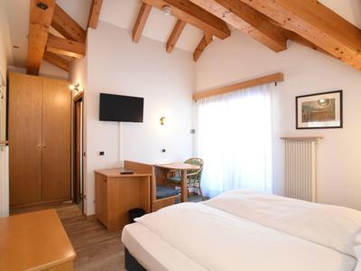 Jasny pokój hotelowy z drewnianymi belkami, podwójnym łóżkiem, biurkiem i telewizorem przy oknie.