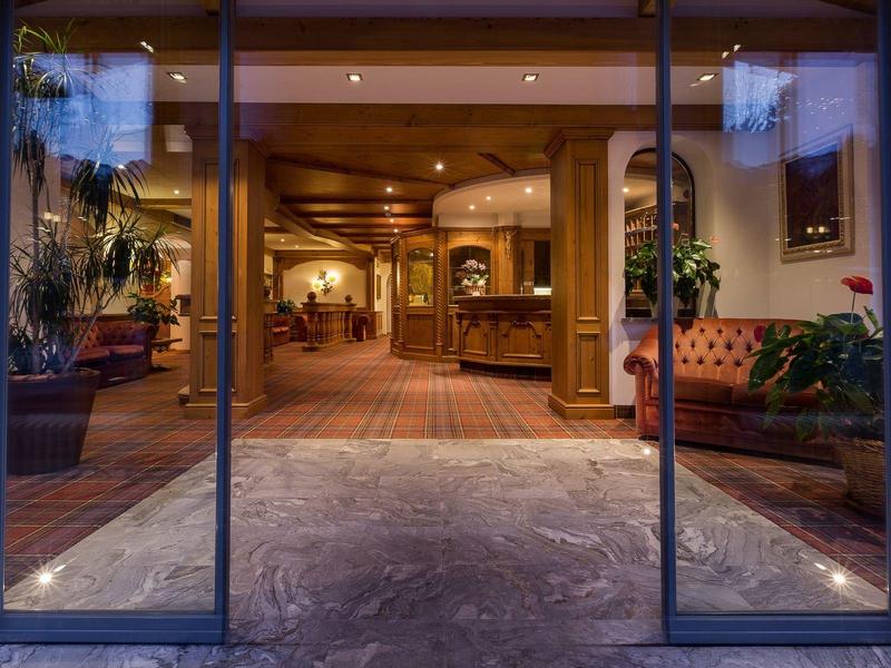 Wejście do lobby hotelowego z przeszklonymi drzwiami automatycznymi, roślinami i miejscami do siedzenia.