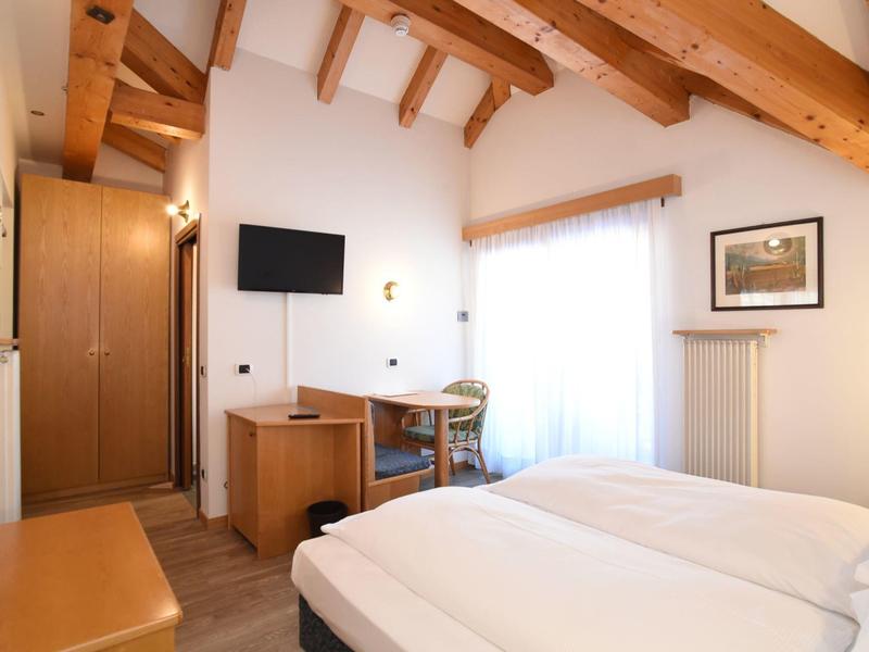 Jasny pokój hotelowy z drewnianymi belkami, podwójnym łóżkiem, biurkiem i telewizorem przy oknie.