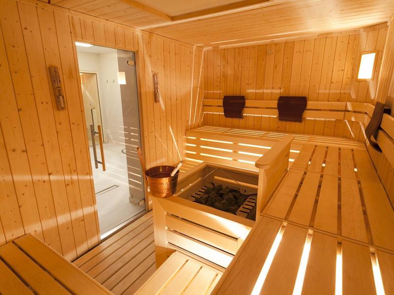 Jasna sauna z drewnianymi panelami, drewnianymi ławkami i otwartym piecem w środku.