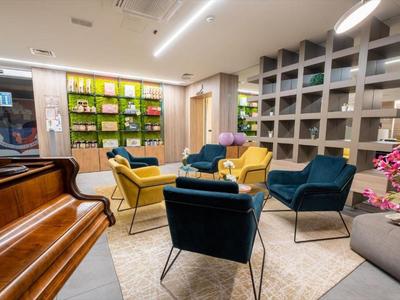 Salon d'hôtel moderne avec groupes de sièges, piano et étagères aux tons sobres.