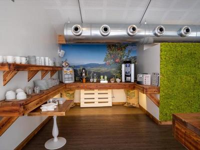 Salle commune moderne avec meubles en bois, machine à café et revêtement mural vert frais.