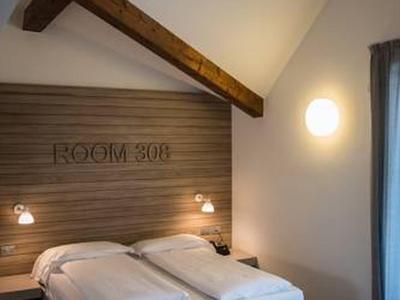 Lit double confortable dans une chambre moderne avec poutres en bois et éclairage dimmable.