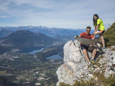 Deux randonneurs se détendent sur un rocher avec vue sur une vallée et des montagnes en arrière-plan.
