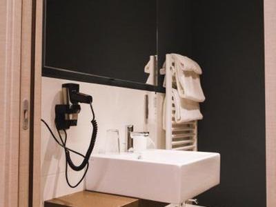 Salle de bain moderne avec lavabo mural, miroir, sèche-cheveux et serviettes sur un mur sombre.