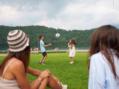 Deux femmes sont assises sur l'herbe pendant que deux personnes jouent au football en arrière-plan.