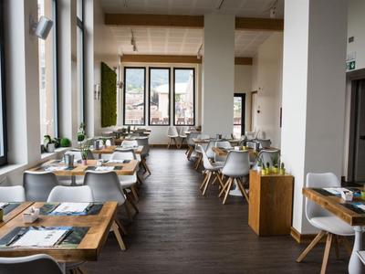 Restaurant moderne et lumineux avec des tables en bois, des chaises blanches et de grandes fenêtres avec vue.