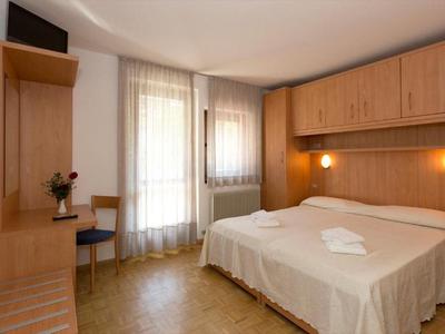 Una stanza d'hotel semplice con due letti, mobili in legno e una finestra con tende.