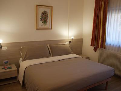 Gemütliches Doppelbett im Hotelzimmer mit Nachttisch und einem Fenster mit Vorhängen.