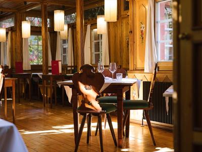 Ein gemütlicher Gastraum mit Holzmöbeln, warmem Licht und gedeckten Tischen bei Tageslicht.