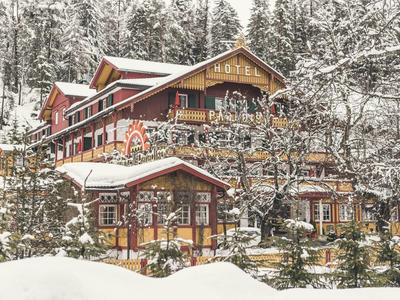 Ein verschneites Hotel in einem Winterwald mit Tannenbäumen und rustikaler Holzarchitektur.
