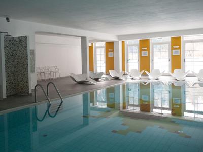 Innenpool mit Liegestühlen und großen Fenstern in einem Hotelbereich.