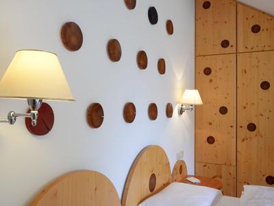 Helles Schlafzimmer mit Holzmöbeln, Wandlampen und dekorativen runden Holzdetails an der Wand.