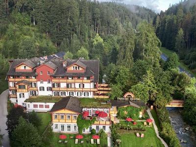 Hotelanlage mit traditionellen Gebäuden und großem Garten umgeben von bewaldeten Hügeln.