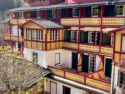 Mehrstöckiges Hotelgebäude mit Balkonen und Wald im Hintergrund bei klarem Himmel.