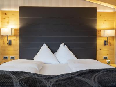 Chambre d'hôtel moderne avec grand lit, tête de lit sombre et boiseries.