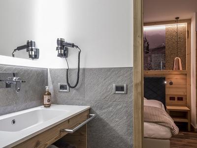 Salle de bain moderne avec baignoire, robinets muraux et sèche-cheveux dans une chambre d'hôtel chaleureusement éclairée.