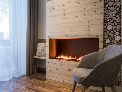 Chambre moderne avec cheminée intégrée, fauteuil gris et sol en bois près d'une fenêtre avec rideaux.