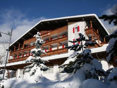 Bâtiment d'hôtel enneigé avec balcons et sapins en hiver.