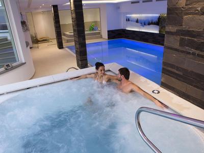 Deux personnes se détendent dans un jacuzzi à côté d'une piscine intérieure dans un espace bien-être.