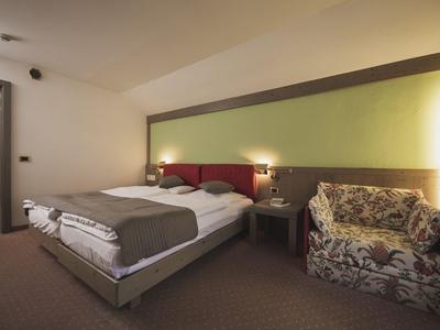 Modernes Hotelzimmer mit Doppelbett, Nachttischen und gemütlichem Sessel, gedämpftes Licht.